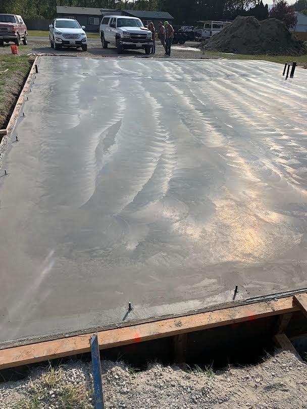 Freshly poured wet concrete driveway with vehicle and equipment visible in background on construction site