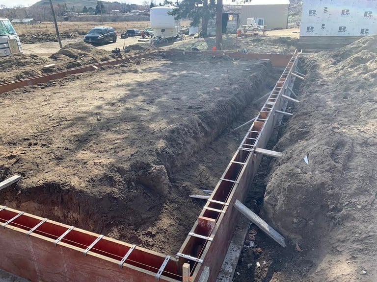 Construction site with deep excavated trench, metal ladders, and buildings in background