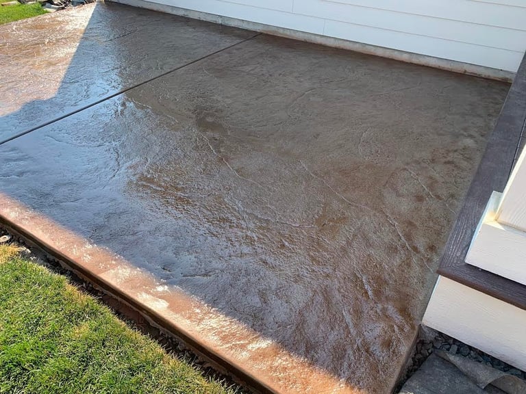 Wet concrete patio or deck area next to white building wall with green lawn visible on left side