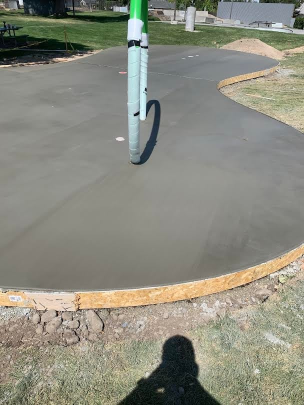 Fresh concrete pour in circular pad with green and white pole and black hose, residential driveway area under construction